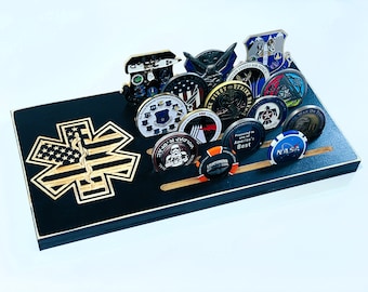 May include: A black wooden challenge coin display featuring a laser-cut Star of Life emblem and slots for holding various challenge coins. The display holds multiple coins with military and other themed designs.