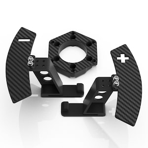 Puede incluir: Un juego de dos levas de cambio de fibra de carbono negra con pernos plateados y símbolos de más y menos en blanco, acompañado de una placa de montaje hexagonal a juego con una abertura circular central y orificios.