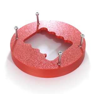 Könnte beinhalten: Ein rotes, kreisförmiges Objekt mit strukturierter Oberfläche und einer einzigartigen Aussparungsform. Vier silberne Bolzen sind gleichmäßig um den Umfang verteilt. Das Objekt befindet sich vor einem weißen Hintergrund.