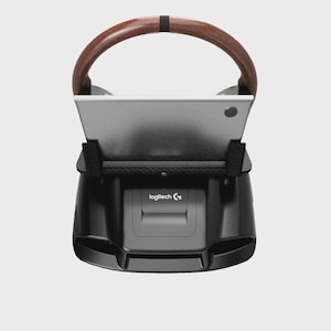 Op de afbeelding: Een zwarte Logitech racestuurvoet met een zilveren metalen middenplaat en een gebogen handgreep met houtnerftextuur. De unit heeft een centrale zwarte behuizing met het Logitech-logo in het wit en twee zwarte zijsteunen.