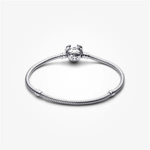 May include: A silver bracelet with a round clasp featuring a decorative design. The bracelet has a snake chain design and is displayed on a white background. The bracelet is a piece of jewellery.