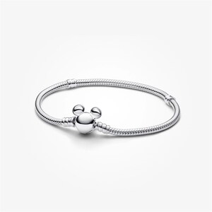 May include: A silver bracelet with a Mickey Mouse-shaped clasp. The bracelet is made of a flexible, snake-like chain. The clasp is a round, polished silver charm with two small round accents above it, resembling Mickey Mouse ears.