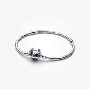 May include: A silver bracelet with a charm depicting Stitch from Lilo & Stitch. The charm has blue, pink, and white enamel details. The bracelet has a flexible, snake chain design. The bracelet is approximately 18 cm in length.