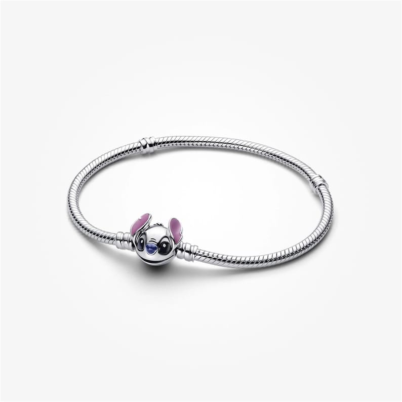 May include: A silver bracelet with a charm depicting Stitch from Lilo & Stitch. The charm has blue, pink, and white enamel details. The bracelet has a flexible, snake chain design. The bracelet is approximately 18 cm in length.