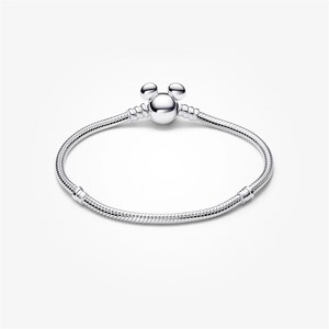 May include: A silver bracelet with a Mickey Mouse-shaped charm. The bracelet has a snake chain design and a round clasp. The charm features three round spheres, two for ears and one for the head. The bracelet is displayed on a white background.