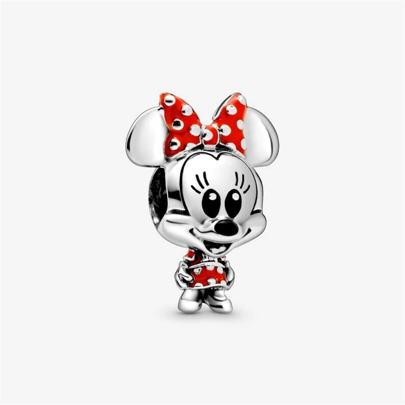 Puede incluir: Un charm de plata que representa a Minnie Mouse. Tiene un lazo rojo con lunares blancos, un vestido rojo con lunares blancos y ojos negros. El charm es un dise&ntilde;o tridimensional.