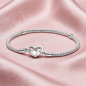Peut inclure: Un bracelet argenté avec un fermoir en forme de cœur. Le bracelet est composé de petites perles rondes et possède un fermoir sécurisé. Le fermoir en forme de cœur est gravé du nom de la marque. Le bracelet est présenté sur un tissu satiné rose.