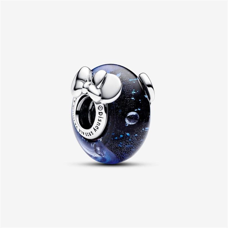 May include: A round charm with a dark blue and black speckled design, featuring a silver bow and two silver Mickey Mouse ears. The charm has the word "Disney" engraved on it.