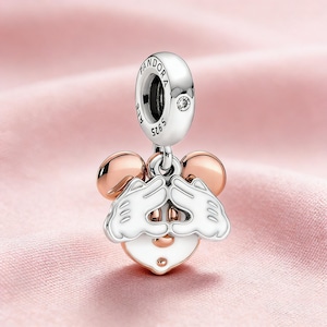 以下が含まれることがあります： ミッキーマウスのデザインのシルバーチャーム。チャームは、Pandoraのロゴと小さな透明な宝石が付いた丸い上部が特徴です。下にはローズゴールドの耳と、白とシルバーのミッキーマウスの顔があります。