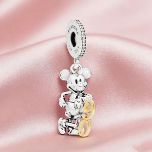 May include: A silver charm featuring Mickey Mouse holding a gold number 90. The charm has a loop at the top with the brand name "Pandora" and "ALE S925" engraved. The charm is designed to be used on a bracelet.