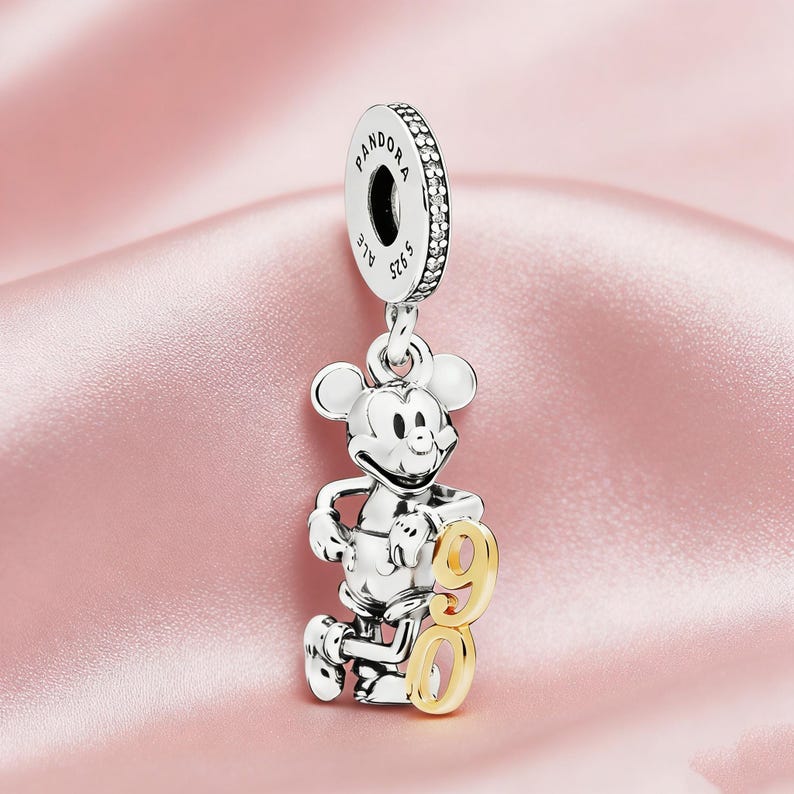 May include: A silver charm featuring Mickey Mouse holding a gold number 90. The charm has a loop at the top with the brand name "Pandora" and "ALE S925" engraved. The charm is designed to be used on a bracelet.
