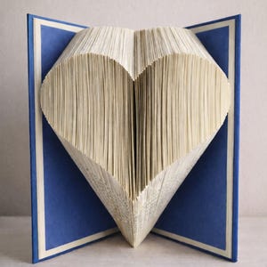 May include: A book with pages folded into a heart shape, displayed open. The book has blue covers and the text "Home Decor DIY" and "No Cutting • No Glue". A creative DIY home decor project.