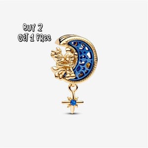 Pode incluir: Berloque dourado com Mickey e Minnie Mouse em uma lua crescente com interior esmaltado azul. Um pingente de estrela com uma pedra preciosa azul pende abaixo. O texto "BUY 2 GET 1 FREE" está no canto superior esquerdo.