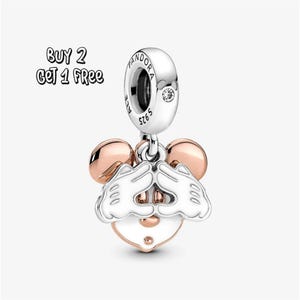 Pode incluir: Um berloque de prata com um design do Mickey Mouse. O berloque apresenta um rosto branco, mãos e um nariz e orelhas em ouro rosa. O berloque tem o texto "S925 ALE" e uma pequena pedra transparente. A imagem também inclui o texto "BUY 2 GET 1 FREE".