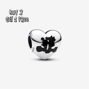 Pode incluir: Um berloque de prata em forma de coração com uma silhueta preta de duas figuras abraçadas. O berloque tem as inscrições "S925" e "PANDORA" gravadas. O texto "BUY 2 GET 1 FREE" está no canto superior esquerdo.