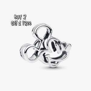 Pode incluir: Um berloque de prata em forma de Mickey Mouse. O berloque é um design tridimensional com um acabamento liso e polido. O texto "BUY 2 GET 1 FREE" está no canto superior esquerdo.