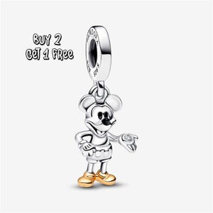 Pode incluir: Um berloque de Mickey Mouse prateado com sapatos dourados e uma pequena gema na mão. O berloque é suspenso por um laço prateado. O texto "BUY 2 GET 1 FREE" está no canto superior esquerdo.
