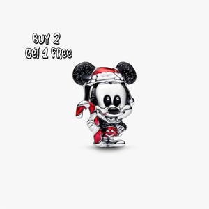 Pode incluir: Um berloque de Mickey Mouse prateado com uma bengala de doces vermelha e branca. Mickey está usando um gorro de Papai Noel e shorts vermelhos. O berloque tem orelhas pretas com manchas brancas. O texto na imagem diz "BUY 2 GET 1 FREE."