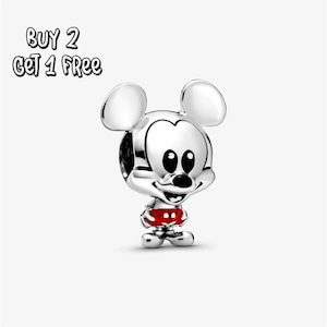 Pode incluir: Um berloque prateado do Mickey Mouse com calções vermelhos com bolinhas brancas. O berloque tem olhos grandes e pretos e uma expressão sorridente. O texto "BUY 2 GET 1 FREE" está no canto superior esquerdo.