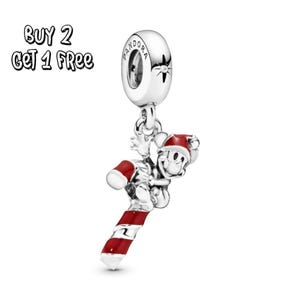 Pode incluir: Um berloque de prata com um design do Mickey Mouse. Mickey está usando um chapéu de Papai Noel e segurando um bastão de doces vermelho e branco. O berloque tem um logotipo da Pandora e o texto "BUY 2 GET 1 FREE".