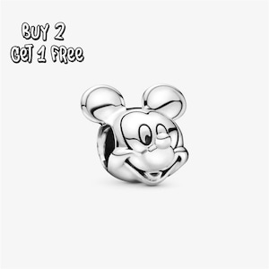 Pode incluir: Um berloque prateado do Mickey Mouse com detalhes em preto. O berloque apresenta o rosto e as orelhas icônicas do Mickey. O texto "BUY 2 GET 1 FREE" está no canto superior esquerdo. Este berloque é colecionável.