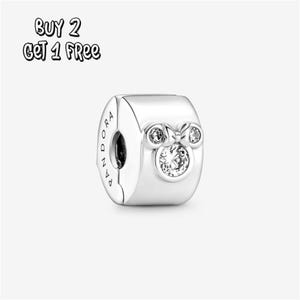 Pode incluir: Um charm de prata com um design da Minnie Mouse. O charm apresenta um cristal grande, redondo e transparente no centro, rodeado por cristais menores e um laço. A palavra "Pandora" está gravada na lateral. O texto "BUY 2 GET 1 FREE" está no canto superior esquerdo.