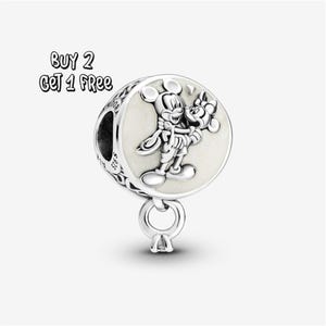 Pode incluir: Um berloque de prata com um design de Mickey e Minnie Mouse. O berloque tem um centro redondo esbranquiçado com os personagens em relevo. O texto "BUY 2 GET 1 FREE" está no canto superior esquerdo. Um pequeno laço e um pingente pendem da parte inferior.