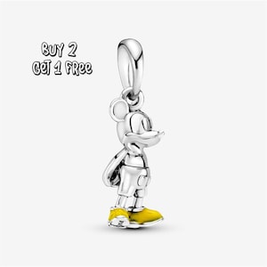 Pode incluir: Um berloque prateado em forma do Mickey Mouse, com sapatos amarelos. O berloque é uma figura tridimensional com uma argola no topo para prender a uma pulseira ou colar. O texto na imagem diz "BUY 2 GET 1 FREE."