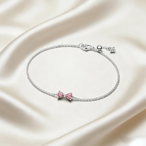 Puede incluir: Una delicada pulsera de plata con un dije en forma de lazo con gemas rosas. La pulsera tiene una cadena fina y un cierre seguro. El dije de lazo es el punto focal, agregando un toque de elegancia a la joyería.
