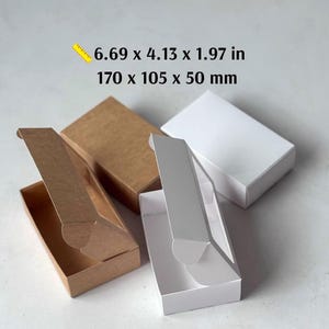 May include: A collection of rectangular cardboard mailing boxes in brown and white. The boxes feature hinged lids and measure 6.69 x 4.13 x 1.97 inches. Some boxes are shown open, while others are closed, displaying their structural design.