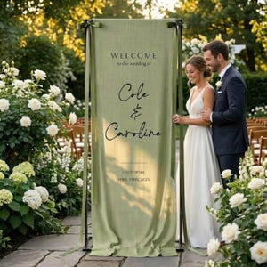Könnte beinhalten: Ein hellgrünes Hochzeits-Willkommensschild mit den Namen "Cole & Caroline" in Schreibschrift. Das Schild wird von einem schwarzen Metallrahmen gehalten. Das Hochzeitsdatum ist der 19. April 2025. Der Text "Willkommen zur Hochzeit von" steht darüber.
