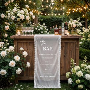 May include: A wooden bar with a white lace runner displaying "The BAR" and a drinks menu, set in a garden. The bar is surrounded by white roses, hydrangeas, and fairy lights. Bottles of spirits and wine are arranged on the bar.