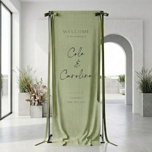 Könnte beinhalten: Ein hellgrünes Hochzeits-Willkommensschild mit schwarzem Text. Auf dem Schild steht „WELCOME to the wedding of Cole & Caroline“ und enthält das Datum „APRIL 19TH, 2025“ und den Ort „CALIFORNIA“. Das Schild ist drapiert und mit grünen Bändern gebunden.