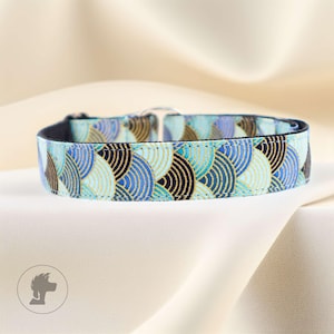 Könnte beinhalten: Ein Hundehalsband mit einem sich wiederholenden Muster aus blauen, schwarzen und goldenen Halbkreisen. Das Halsband hat eine schwarze Innenseite und eine silberne Metallschnalle. Der Hintergrund ist ein weicher, cremefarbener Stoff.