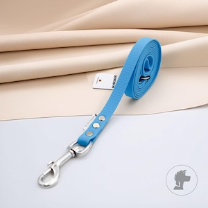Pode incluir: Uma trela para cão azul brilhante com um padrão de favo de mel texturizado na fita, um mosquetão giratório de metal prateado e três rebites prateados. Uma pequena etiqueta retangular branca com o texto DISTINCUSH ME está presa à trela.