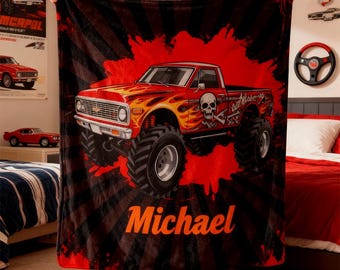 May include: A red and black blanket featuring a monster truck design with flames, a skull, and the name "Michael" in orange. The truck has large tires and is set against a red and black background.