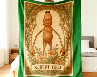 May include: A green plush blanket featuring a central illustration of a brown, humanoid figure with sunglasses, surrounded by floral and Art Nouveau-style design elements. The text "ROBERT, HELP" is displayed on a banner at the bottom.