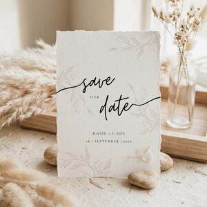 May include: A rectangular off-white card with deckled edges featuring the black text "save our date" in a cursive script. Below the text are the names "KASIE + CADE" and the date "18 | SEPTEMBER | 2026". The card has light gray floral line art.