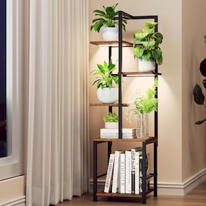 May include: A black metal and wood bookshelf with multiple shelves. The shelves hold potted plants, books, and a glass vase with flowers. The plants are in white and blue pots. The bookshelf is next to a window with a white curtain.
