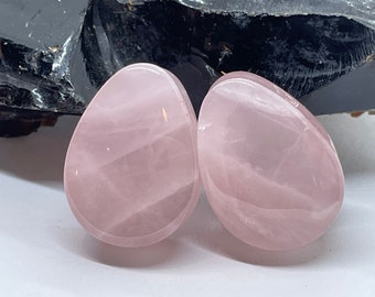 May include: Pair of pink rose quartz stone plugs, each with a smooth, oval shape and a light pink color.