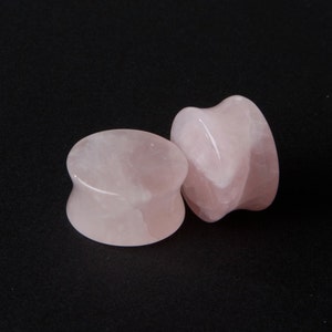 Puede incluir: Dos medidores de oreja de cuarzo rosa, uno es de forma cilíndrica simple y el otro es de forma más orgánica y libre.