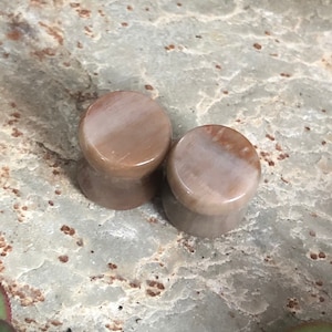 May include: Two brown and white stone ear gauges. The gauges are round and have a smooth, polished finish.