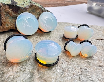 May include: A set of eight opalite ear gauges in various sizes. The gauges are a milky white color with a slight iridescent sheen. They are displayed on a light gray stone surface.