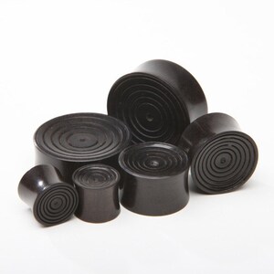 May include: A set of six black wooden ear gauges with a concentric circle design. The gauges are of varying sizes.