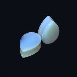 Op de afbeelding: Twee traanvormige opalite-pluggen, een bovenop de andere, tegen een zwarte achtergrond.