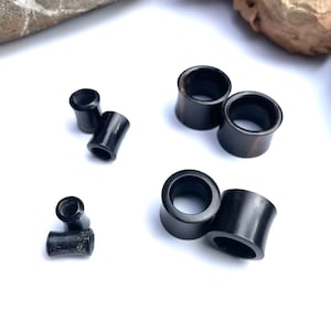 May include: A set of black wood ear gauges in various sizes. The gauges are smooth and polished, with a natural wood grain visible.