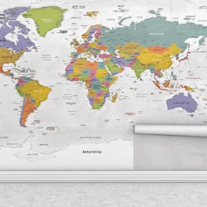 May include: A colourful world map displayed on a wall, with countries in various colours. The map is partially unrolled, revealing a white backing. The map includes the names of countries and oceans. The map is mounted on a white wall above a white skirting board.