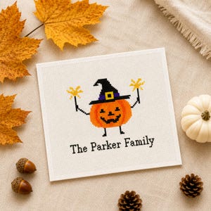 May include: A square white fabric piece featuring a cross-stitch design of an orange jack-o'-lantern wearing a black witch hat with a purple band. The pumpkin holds yellow sparklers in its hands. The text The Parker Family is stitched below.