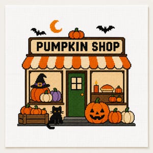 Puede incluir: Un patrón de punto de cruz que muestra una tienda con el letrero PUMPKIN SHOP y un toldo a rayas naranjas y blancas. La escena incluye una puerta verde, un gato negro, varias calabazas en naranja, blanco y morado, murciélagos y una luna creciente.