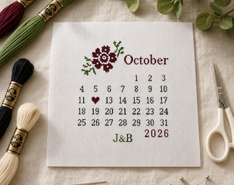 Op de afbeelding: Een witte vierkante kruissteekstof met een kalender voor oktober 2026. Het ontwerp bevat een donkerrood bloemmotief, de tekst "October", het jaar "2026", de initialen "J&B" in het groen en een klein rood hartje op de 12e dag.